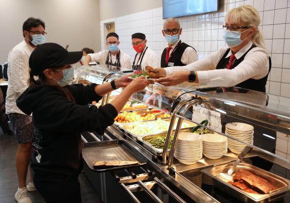 A canteen servery with people being handed plates of food