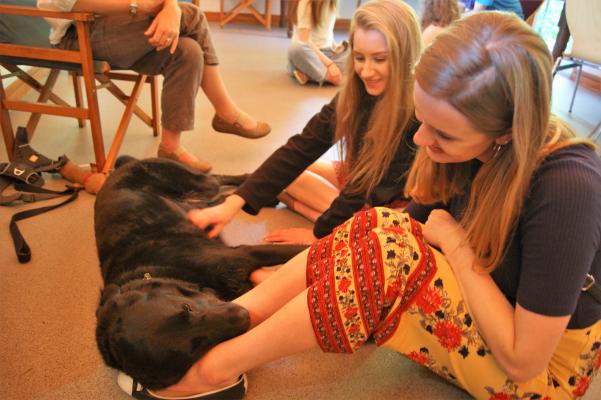 Two students sitting on the floor with a Labrador 