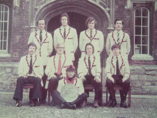 Colour photo of 1972 First crew in white rowing blazers with black and red trims, holding the Mays plate in First Court, Jesus College