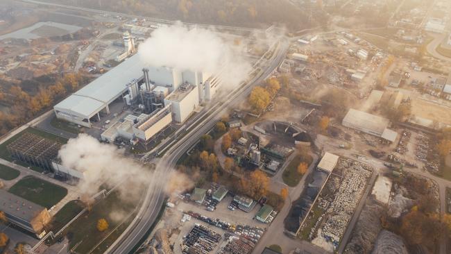 Image of An aerial shot of a power station, with smoke drifting from its chimneys, next to streets with shops and houses.