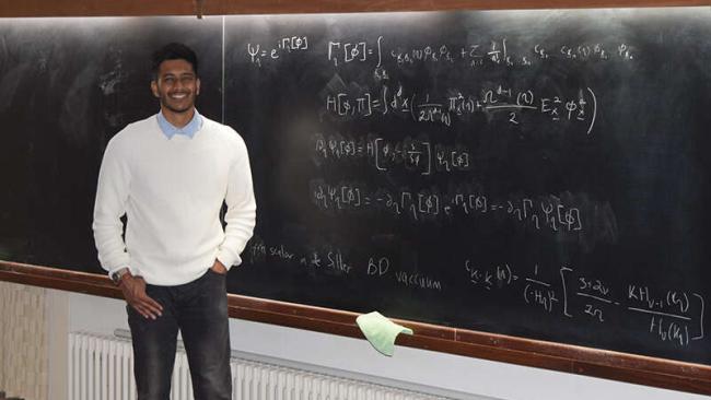 Image of Ayngaran Thavanesan standing by a blackboard with an equation written on it.
