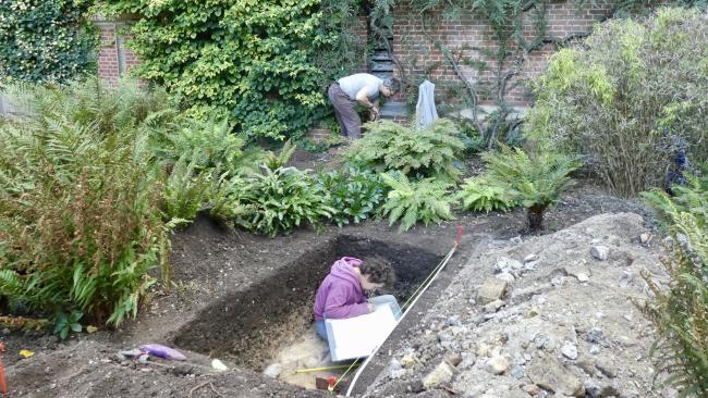 Image of Archaeologists sitting in a trench amongst plants