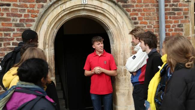 Image of A Jesus College student standing by a door entrance and talking to a group of visitors