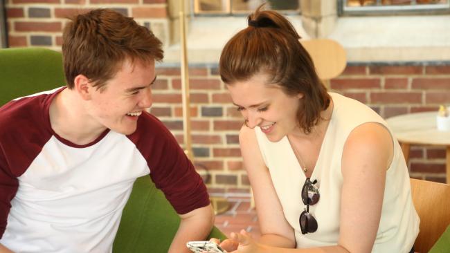 Image of A man and woman sitting in a cafe, smiling and looking at a smartphone