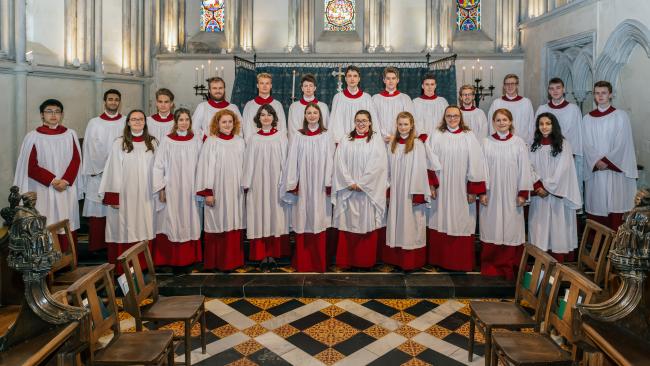 Image of Choir members, wearing robes and standing in the College Chapel