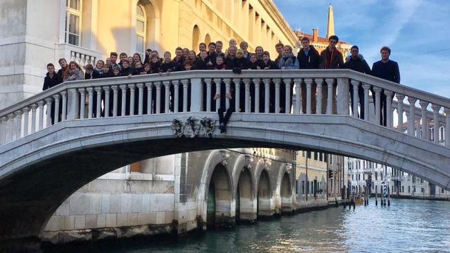 Choir members standing on a bridge over an Italian canal
