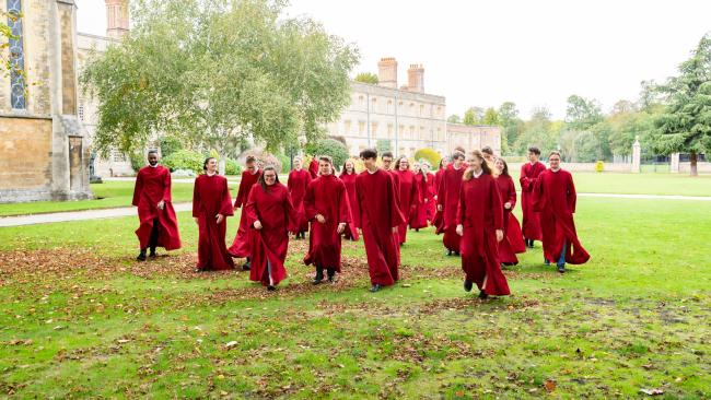 A group of choir members wearing deep red choir robes, walking across a lawn