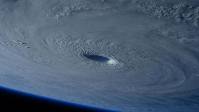 A photograph taken from space showing clouds and a hurricane spiral on Earth