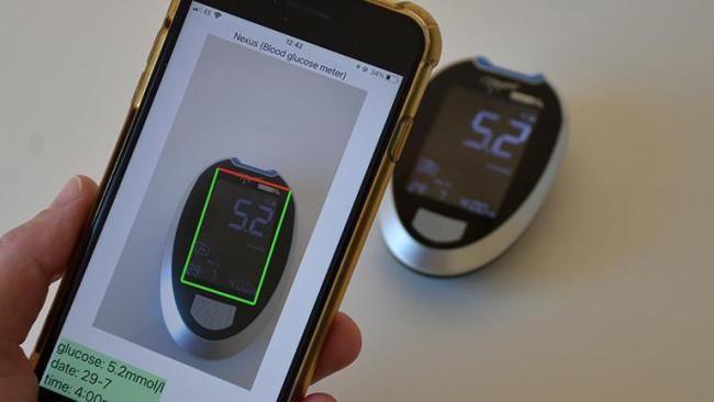 A hand holding a smartphone, the screen shows a scan of a diabetes monitor