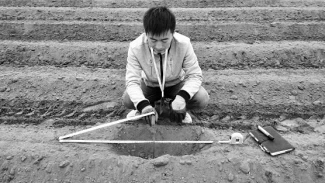 A man measuring a hole in the ground of a ploughed field