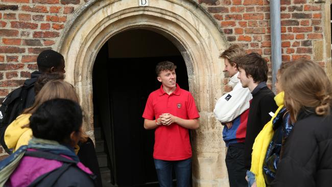 A Jesus College student standing by a door entrance and talking to a group of visitors